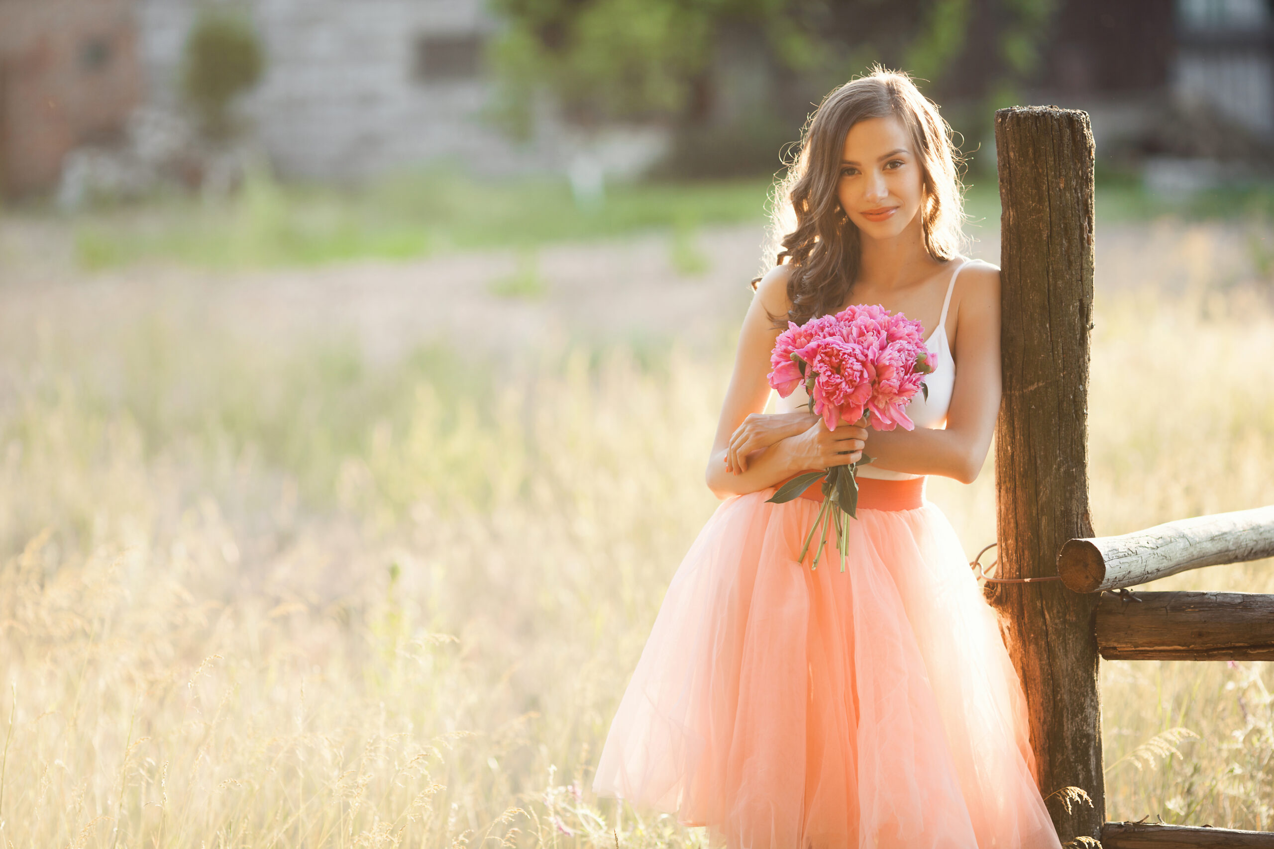 Beautiful young girl with pions on the nature otdoors in the sunshine. Pretty woman outside with flowers in the pink skirt